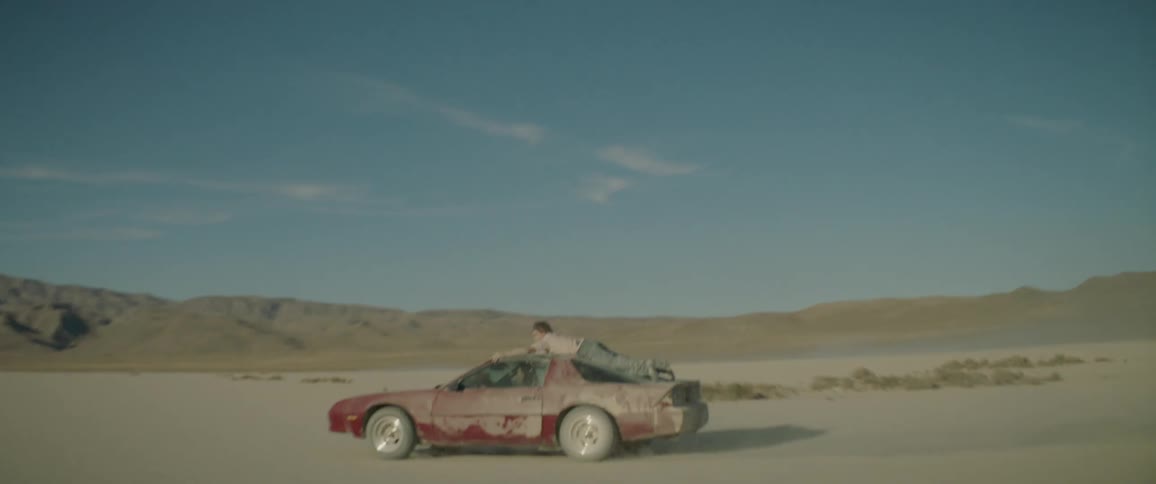 A man rides on the hood of a car as it drives through the dirt