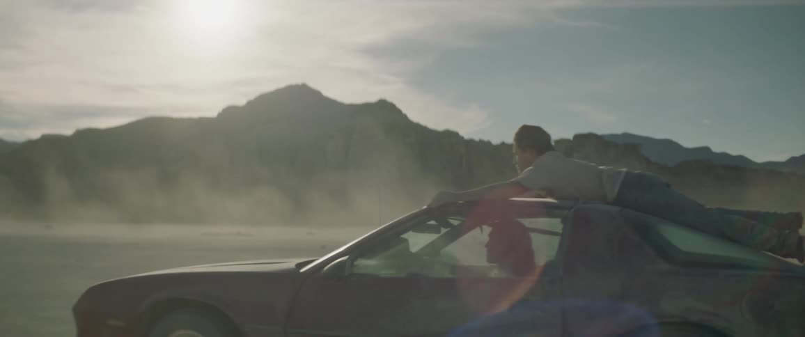 A man hangs on the roof of a car as it speeds off