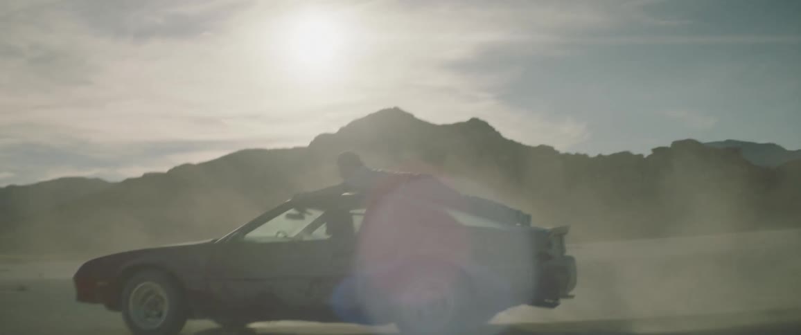A man rides on the roof of a car as it drives through the dirt