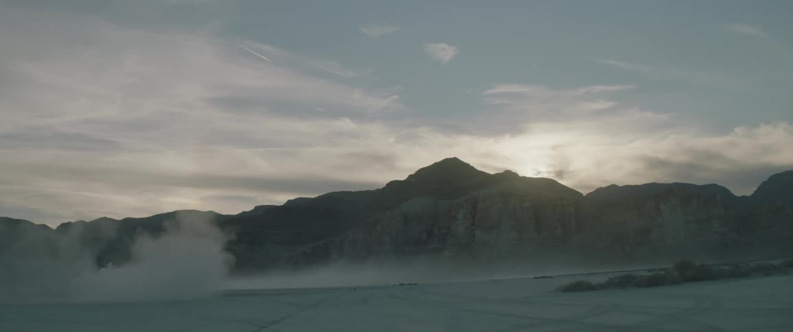 Smoke billows up in front of hills during sunrise