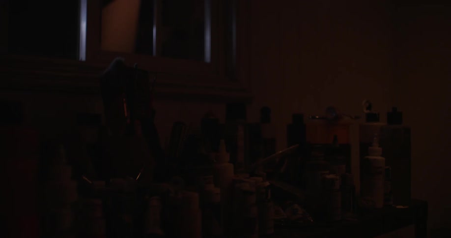 A table in a dark room is crowded with plastic bottles of lotions and creams