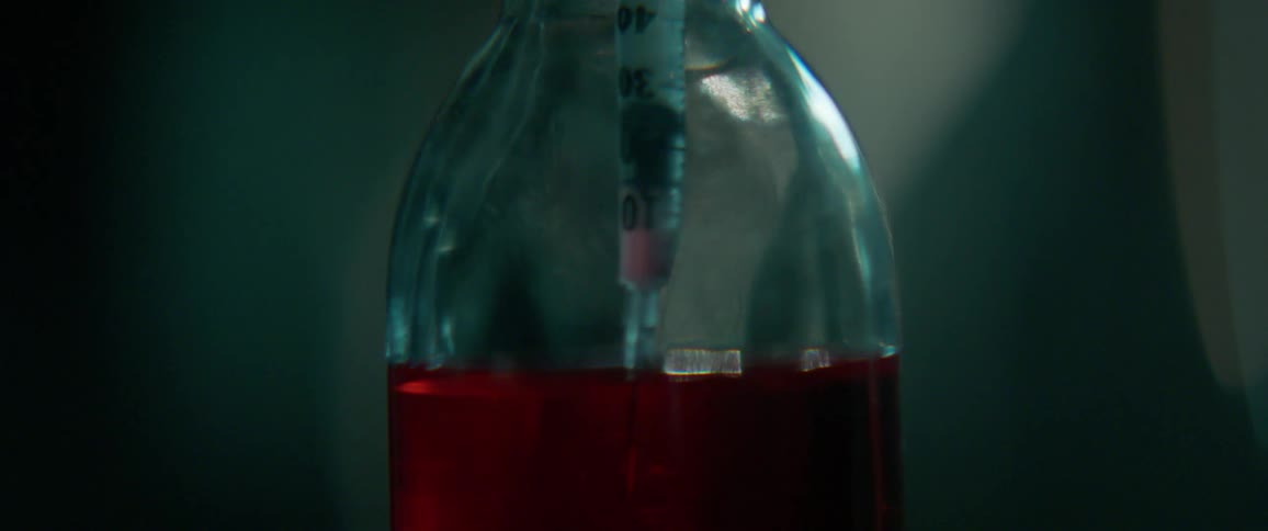 A syringe is dipped into a vial of red liquid