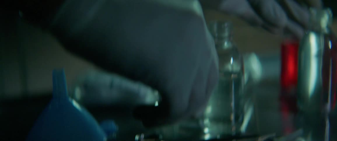 A man wearing latex gloves sets down scissors and picks up a jar