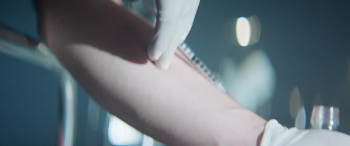 A man wearing latex gloves is injecting himself using a hypodermic needle