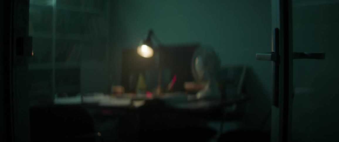 A desk light on a desk is being filmed from the doorway of an office