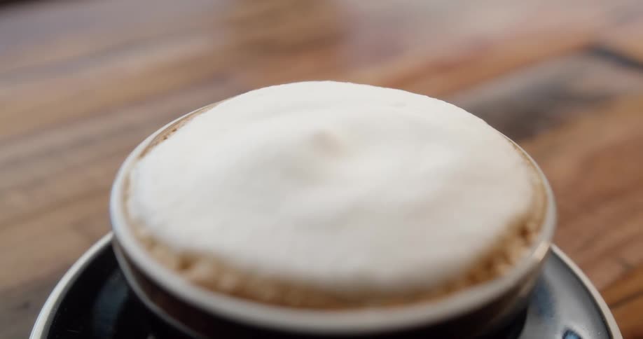 Foam topped coffee fills dark ceramic cup resting on saucer net to spoon