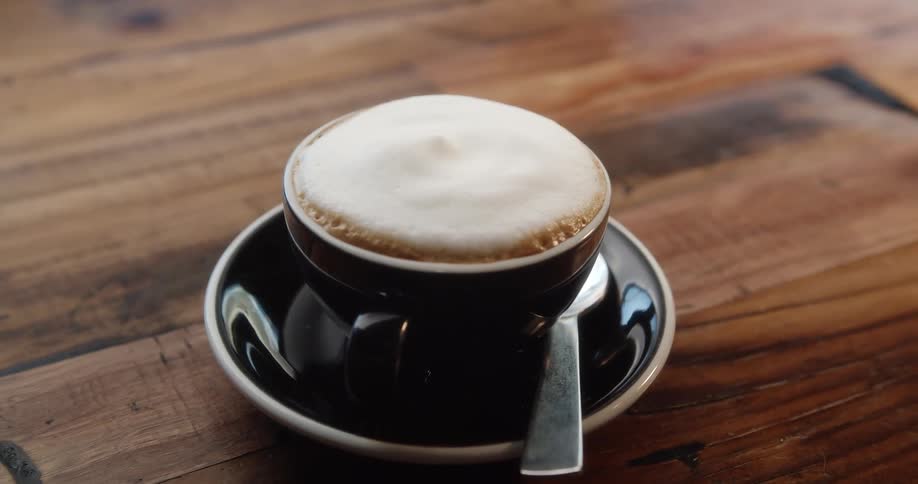 Foam tops coffee in cup sitting on saucer next to spoon on table