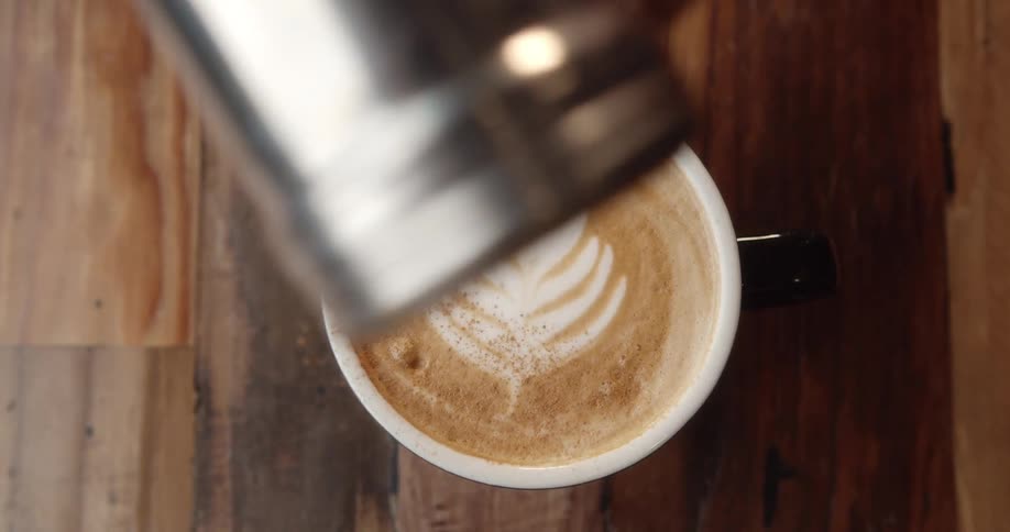 A person sprinkles chocolate on top of a coffee in a restaurant