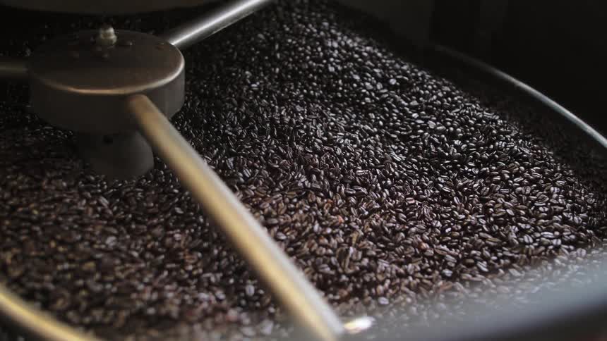 Thousands of whole coffee beans are stirred and spun in a large receptacle