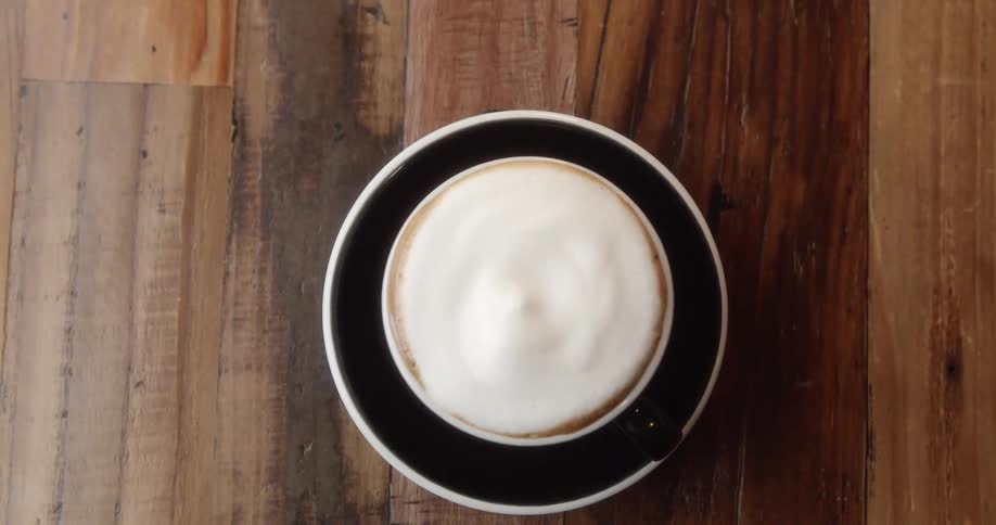 A person puts a coffee cup over a dish with a spoon