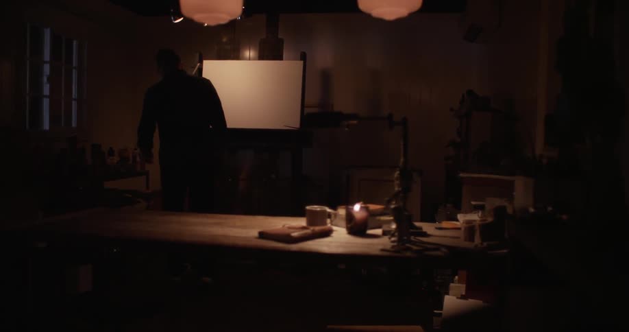 A man stands before a blank canvas on an easel and then walks away