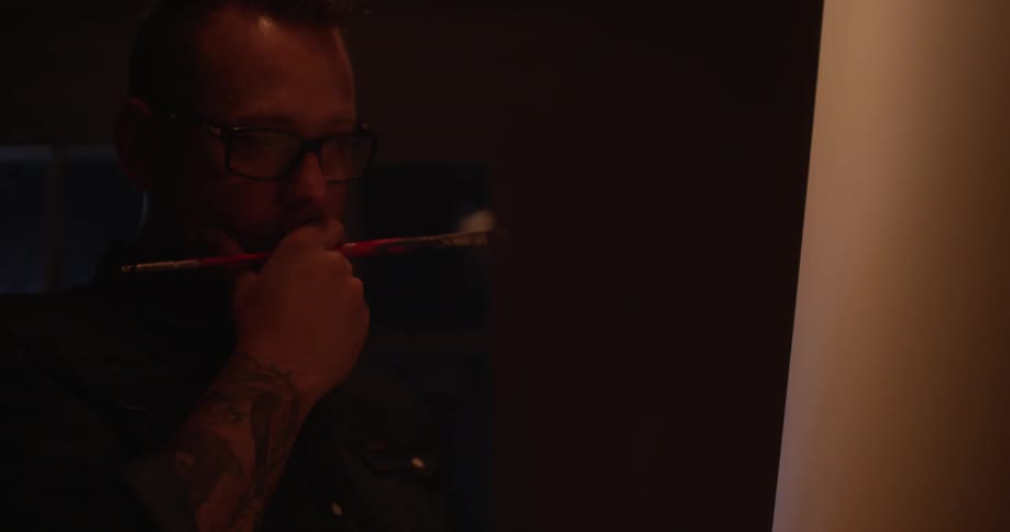 A man is painting on a canvas in a dark area