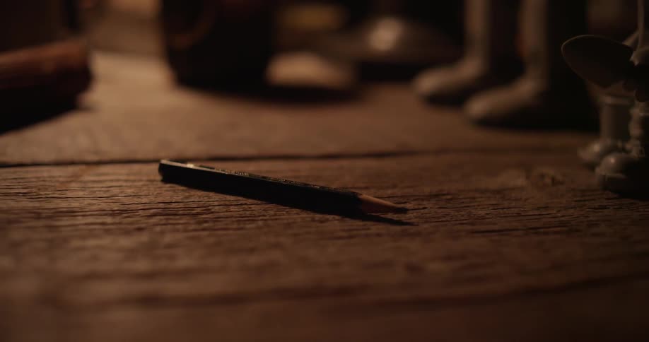 A person picks up a pencil from a wooden table