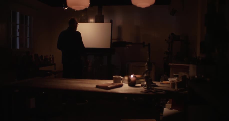 A man standing in front of an easel and blank canvas having trouble starting his work