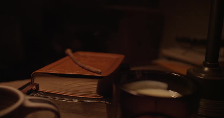 A candle flickering and blown out as it sits on a desk with books and knick knacks