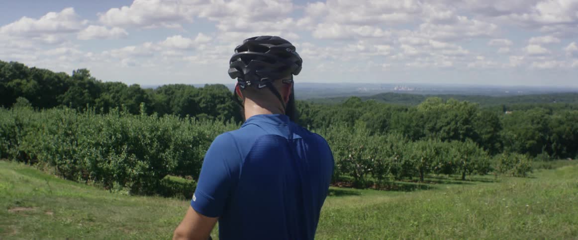 A man wearing a bike helmet overlooks a grove