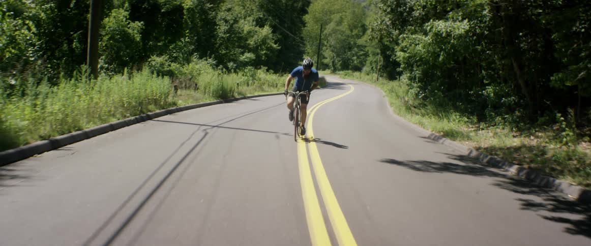 A bicyclist pedals down a rural road on a sunny day