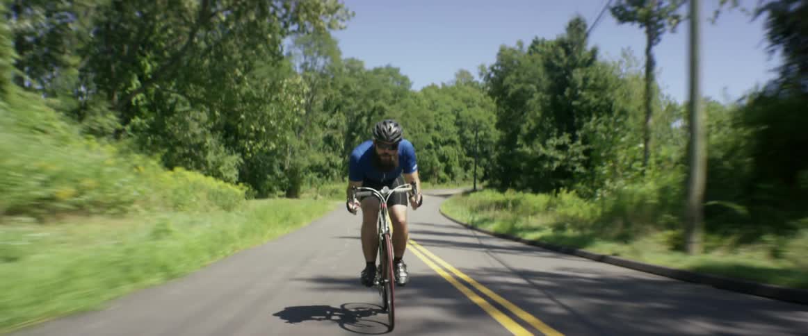 A bearded man riding a racing bicycle quickly down a two lane road