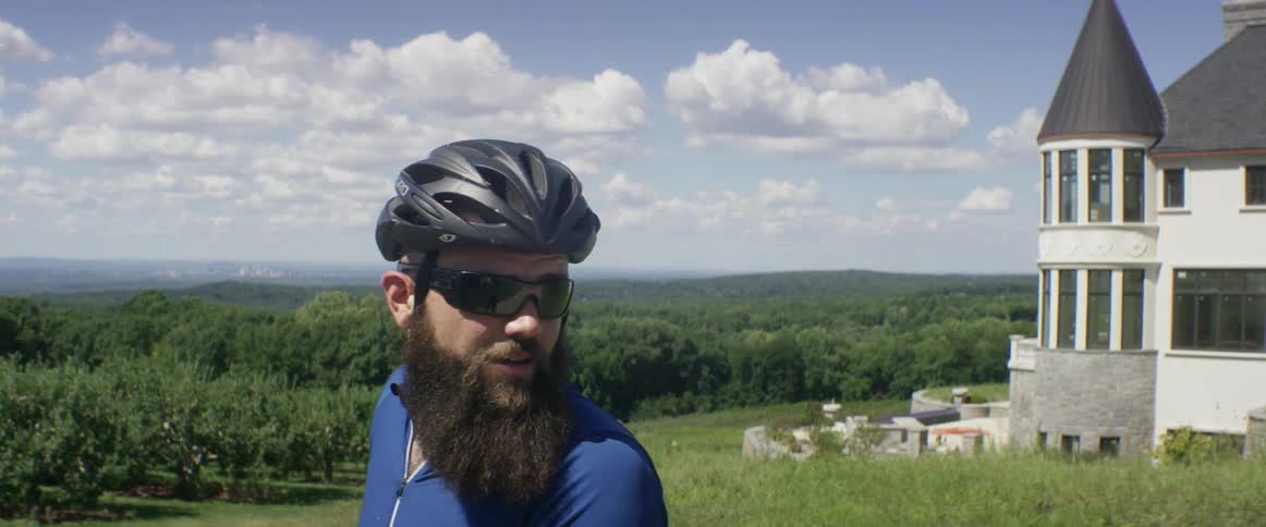 A man wearing sunglasses and a bicycle helmet turning to look over his shoulder