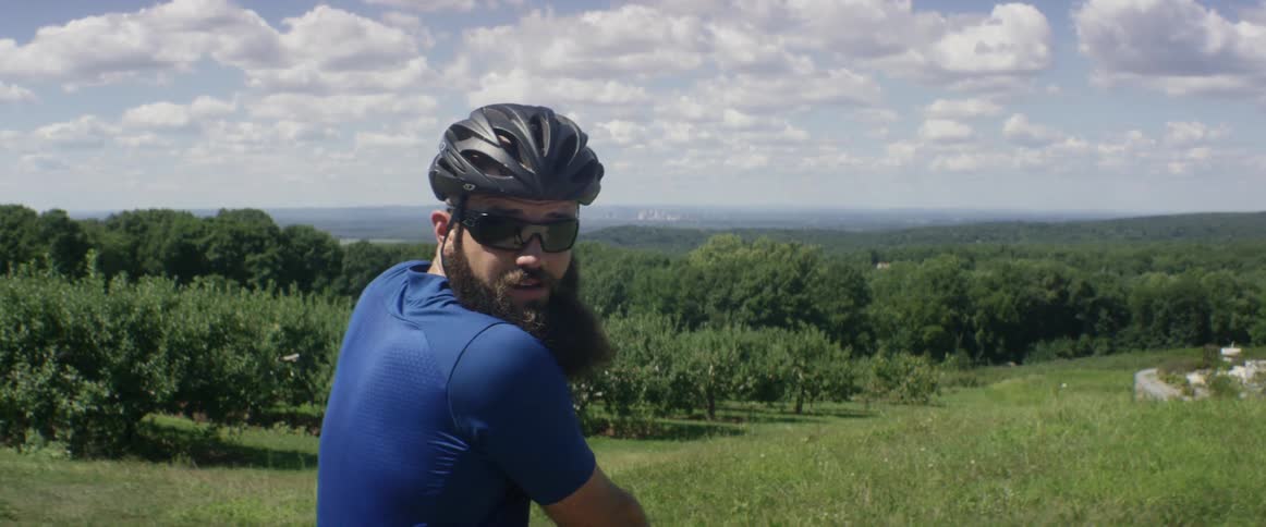 A man wearing a helmet turns around before a dense forest