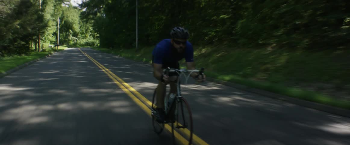 A bearded man riding a racing bicycle quickly down a rural two lane road