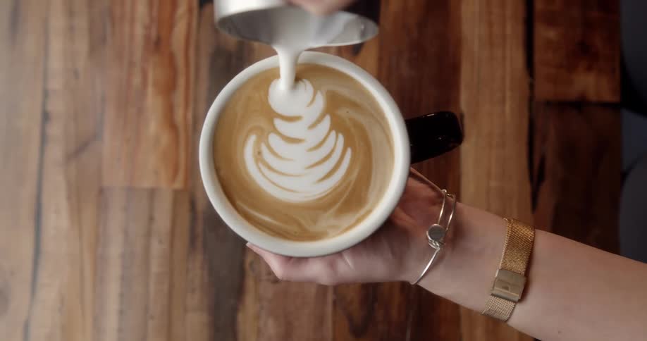 Barista makes a latte art leaf over a wooden table