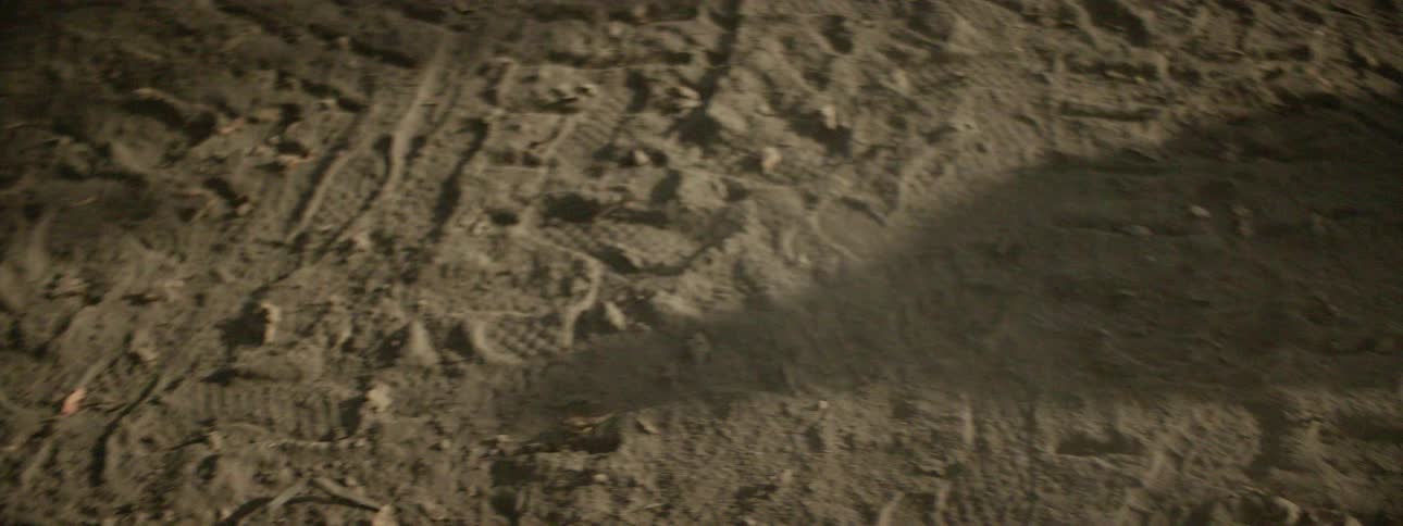 Human walks across the dirt and kicks up dust while casting a shadow