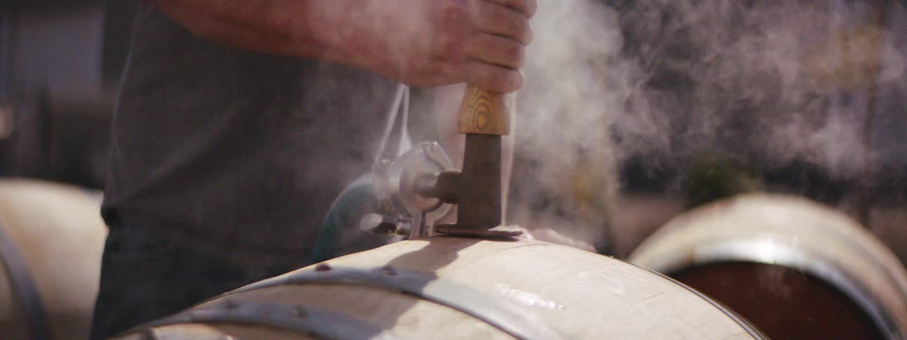 A person putting a tool with steam and a hose in a barrel