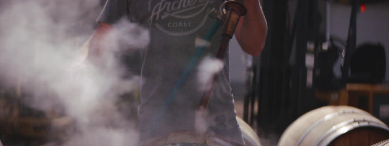 Man uses a too to fill wooden barrels with steam and plugging the hole with a cork