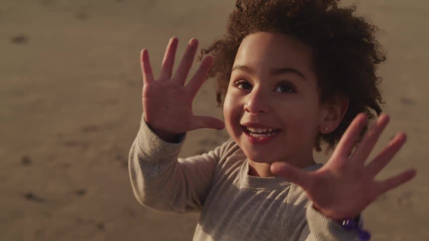 Little boy smiles and shows his extended hands while standing on the sand of a beach at sunset