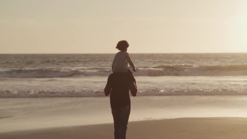 A father walking on the beach with his daughter on his shoulders