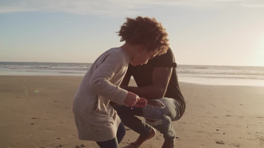 Young child picks something up from the beach and shows it to a man who is crouching