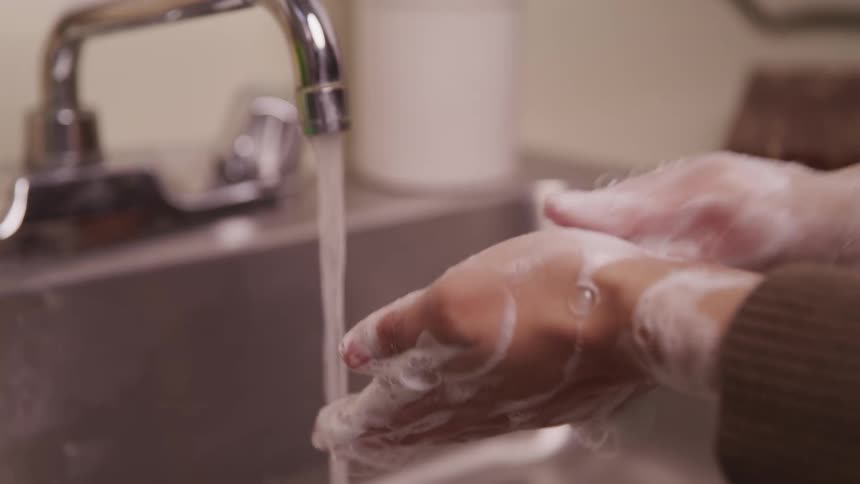 A person washing their hands with soap by a sink