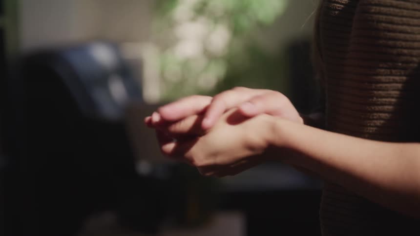 A woman standing inside her home rubs her hands together
