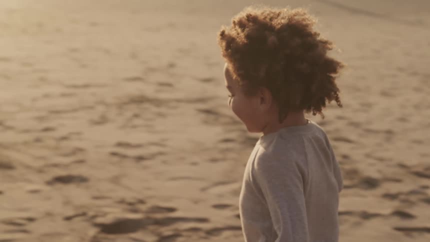 A child runs through the sands of a beach as an adult watches from nearby