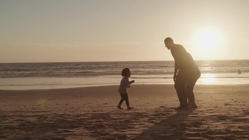 A toddler runs to her mom and dad as they play on the beach