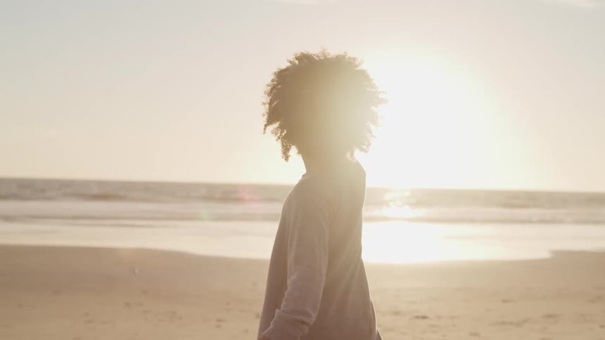 A boy standing and smiling on a beach with the ocean and the sky in the background