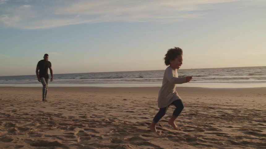 A young smiling boy runs along a beach as his mother runs along behind and his father follows at a slower pace