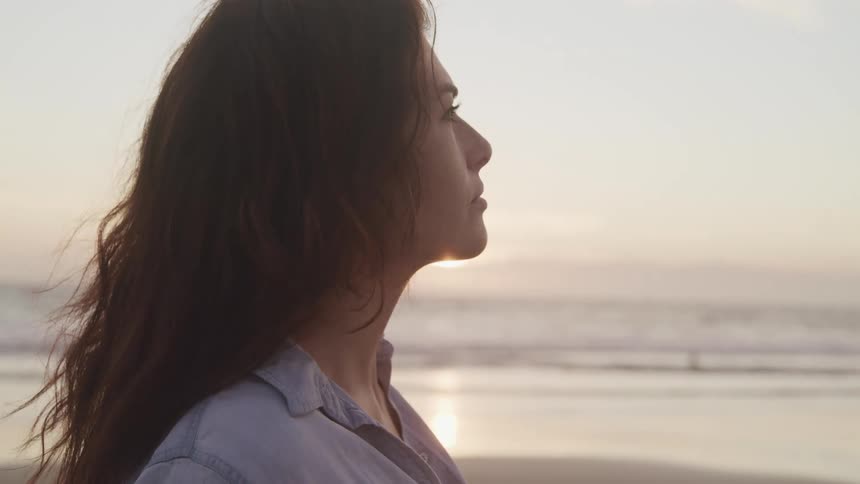 A caucasian female standing near the ocean looking ahead
