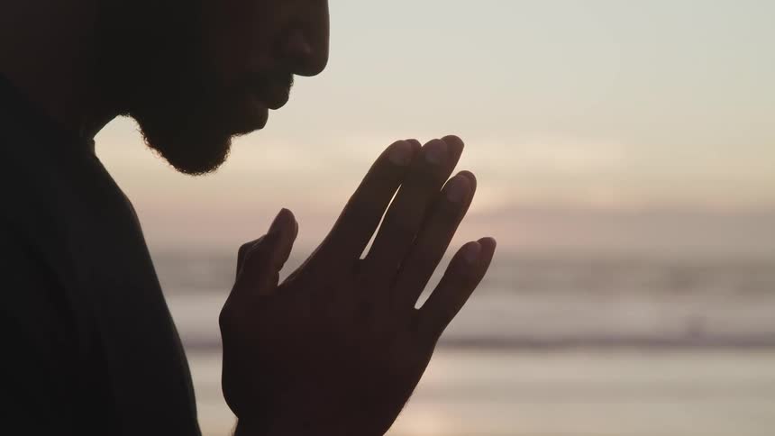A black male standing at a beach praying