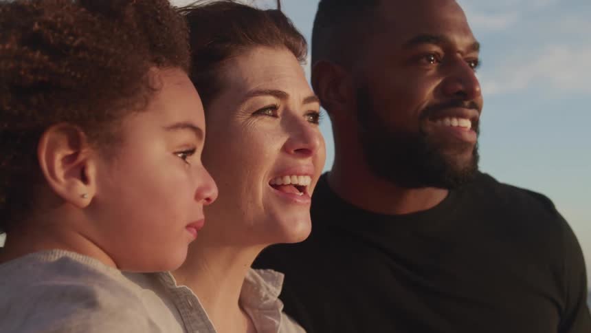 A man and woman stand together as the woman carries a girl and the three of them look at something out of frame