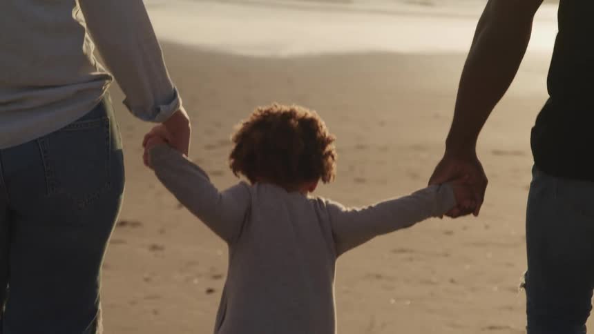 A child walking in a beach holding hands with his mother and father