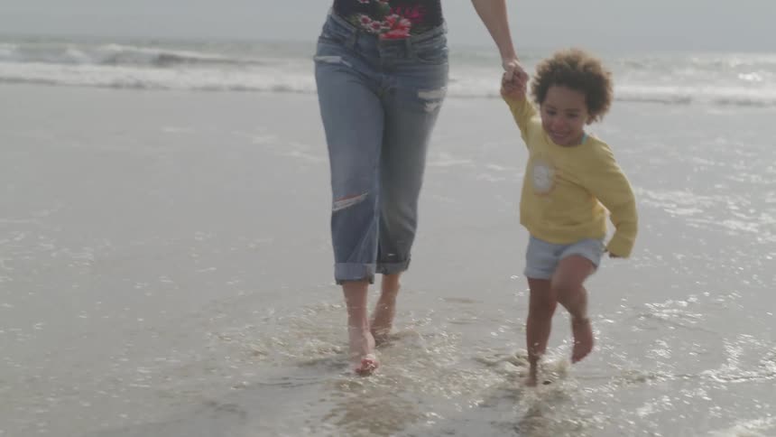 A woman holds the hand of a small child as they play on the beach by running in place in the low tide