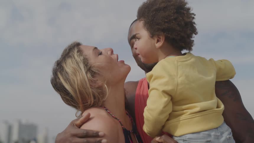 An couple with their toddler hugging and kissing each other