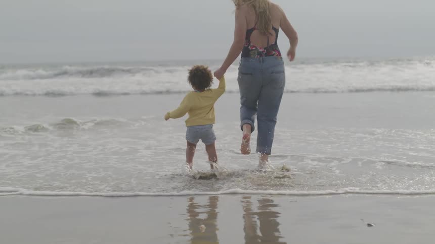 Mother and son run barefoot into the beach shores while holding hands