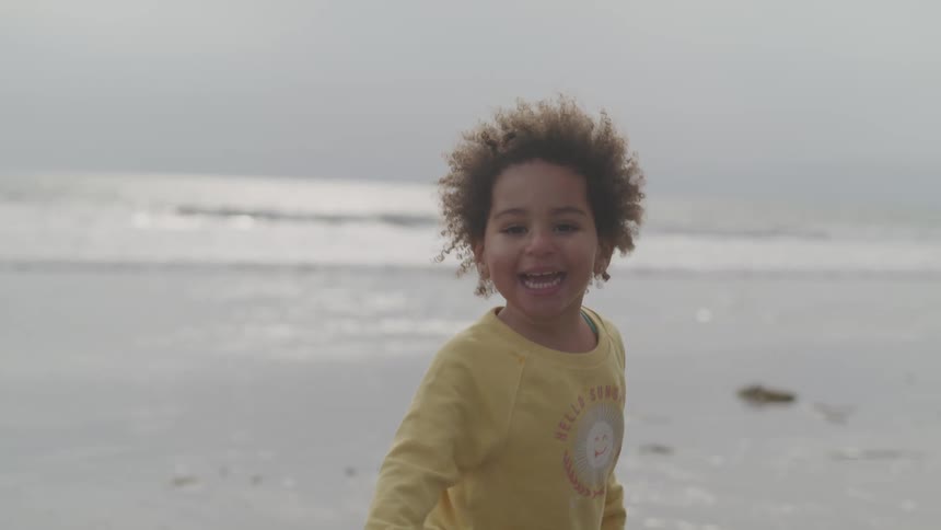 A laughing girl on the beach turns and runs away from the waves
