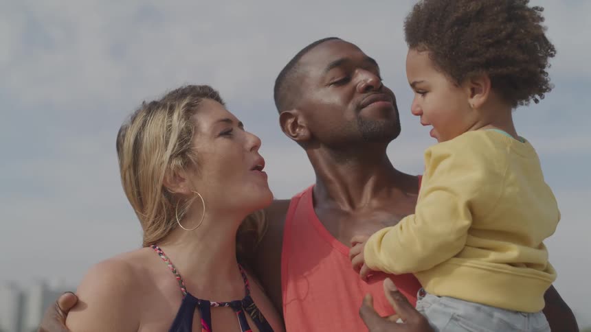 Father and mother smile and kisses son outdoors