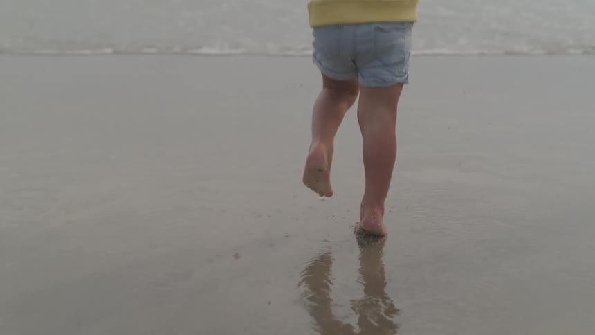 A child runs down the beach with their parent