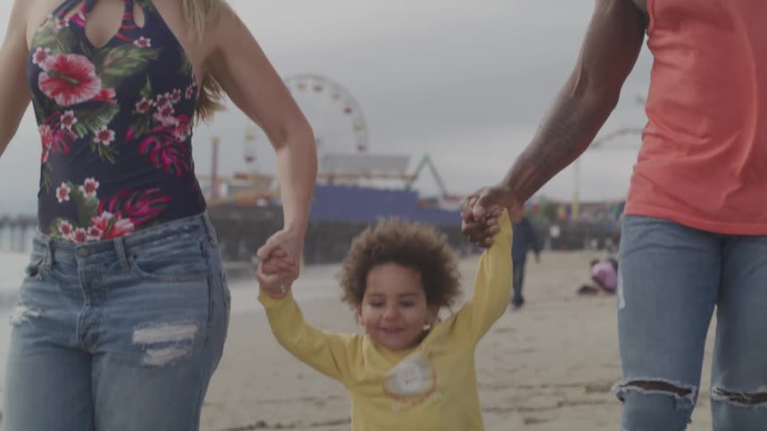 A man and woman lift their toddler together in a swinging motion on the beach