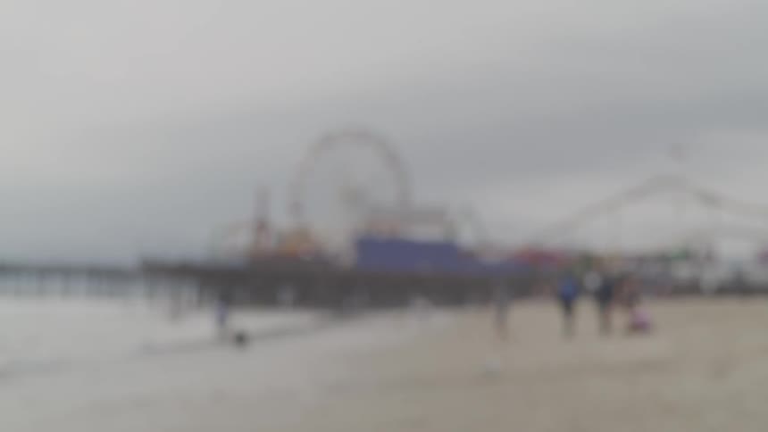 Parents swing laughing child between them as they walk on beach with amusement park in background